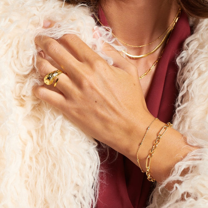 Close-up of a hand wearing gold jewelry with a fluffy white garment.