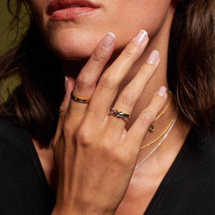 Close-up of a woman's hand with rings and a necklace, touching her face.