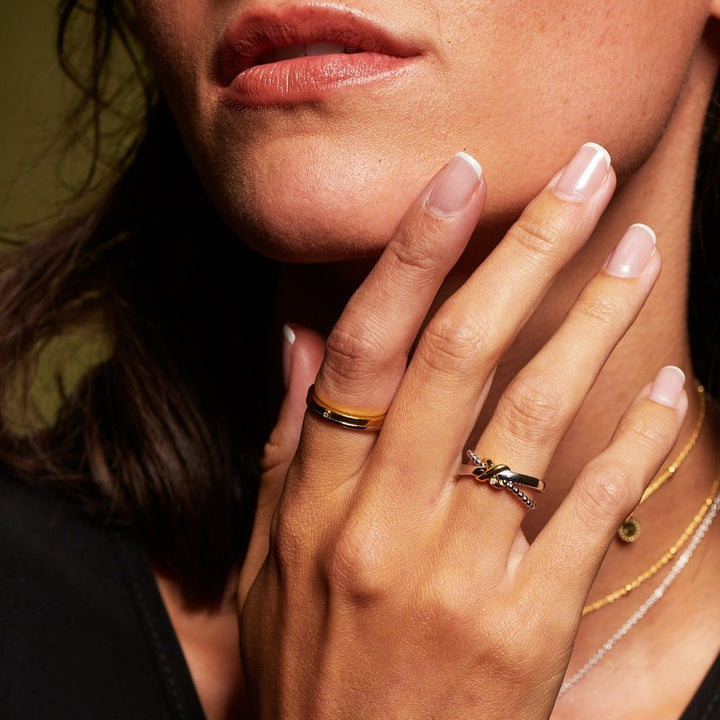 Close-up of a person's hand with rings and a necklace, touching their face.