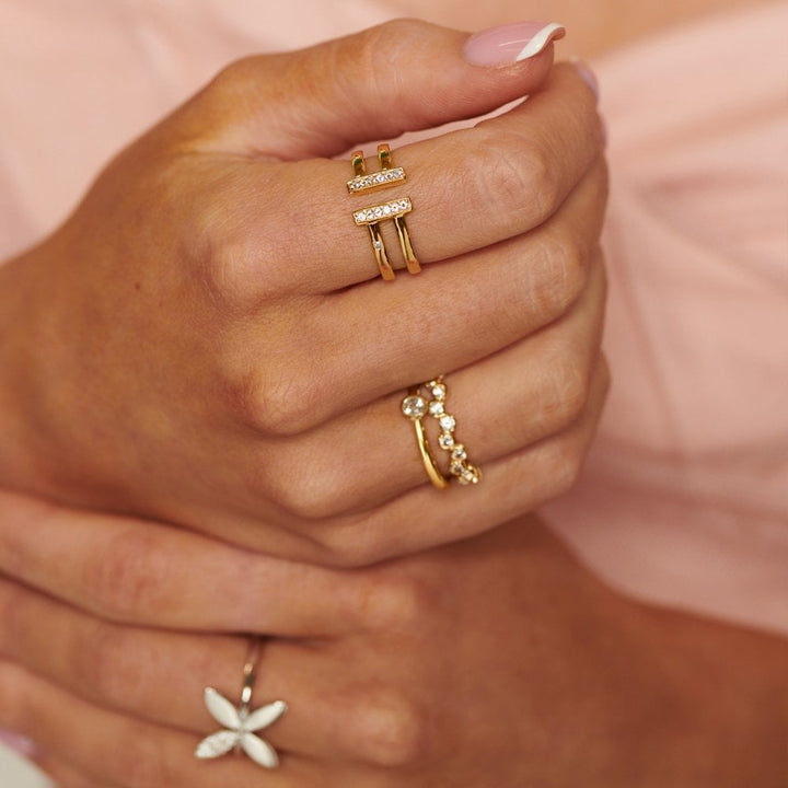 Close-up of a hand wearing gold rings with gemstones on a soft pink background
