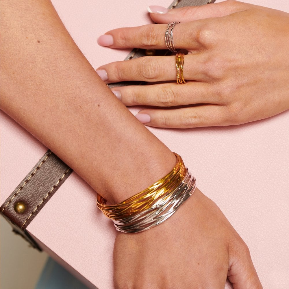 Close-up of hands wearing gold and silver bracelets on a pink background