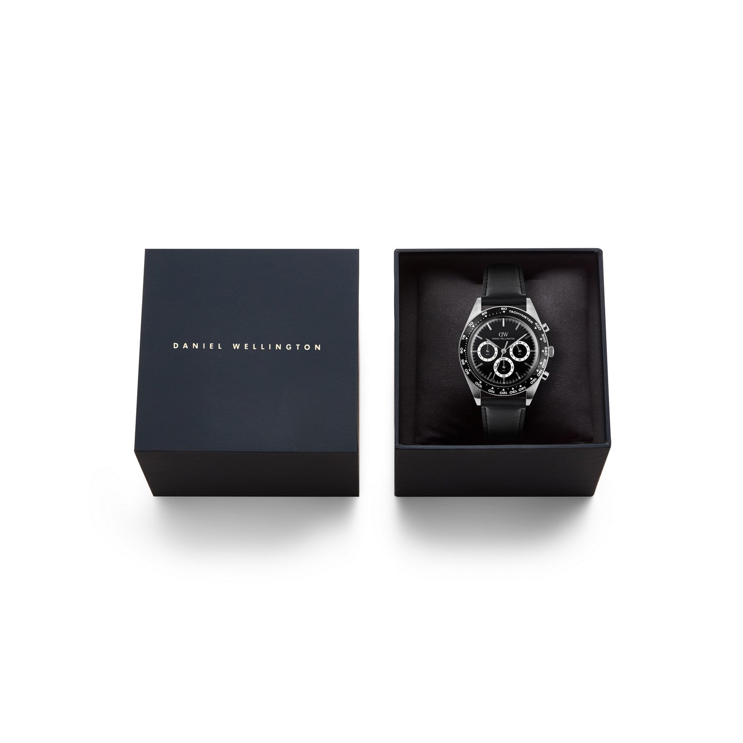 Daniel Wellington black chronograph watch with a black strap, presented in an open black gift box next to its closed lid on a white background.