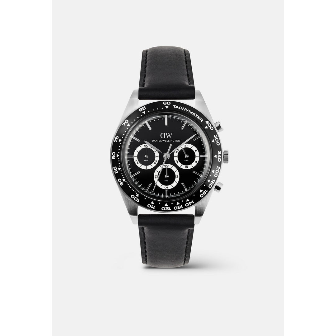 A wristwatch with a black dial, black leather strap, and a silver-toned stainless steel case. The dial features three subdials, a black tachymeter bezel, and the 'DW' logo for Daniel Wellington.