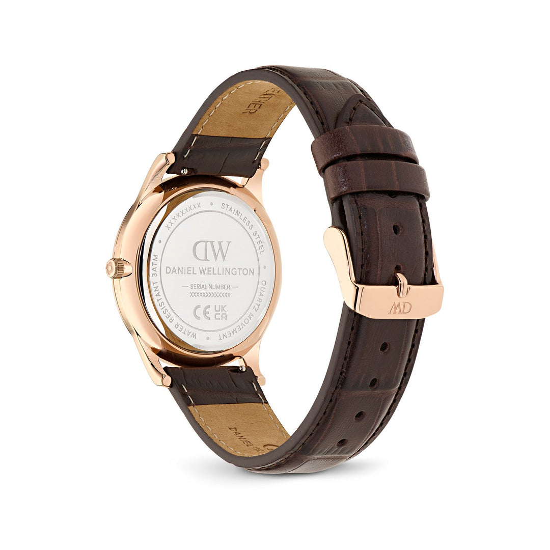 Daniel Wellington watch with a rose gold case and a dark brown leather strap, showing the back of the watch with a clear crystal and the branded clasp on a white background.