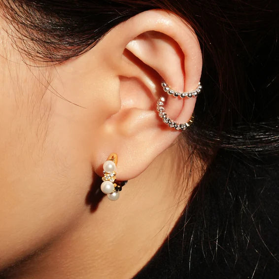 Close-up of an ear wearing gold and pearl hoop earrings with a dark background