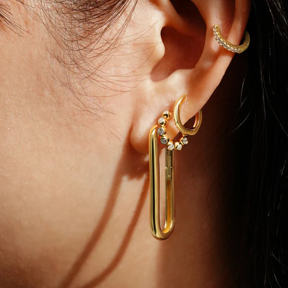 Close-up of a person wearing a gold earring with a small gemstone.