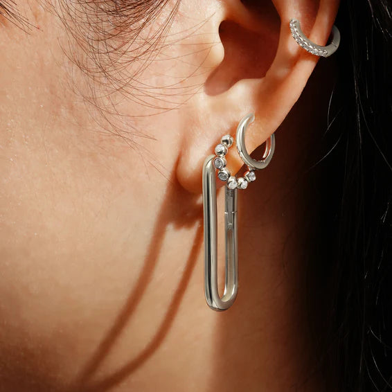 Close-up of a person's ear wearing a silver earring with a unique design.