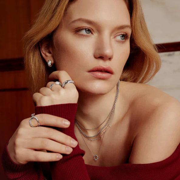 Woman wearing multiple rings and necklaces, holding a red sweater sleeve.