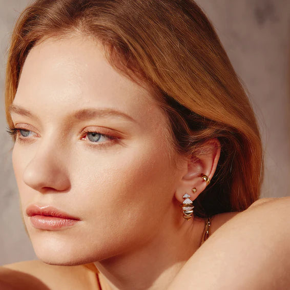 Close-up of a woman wearing gold hoop earrings with a neutral background