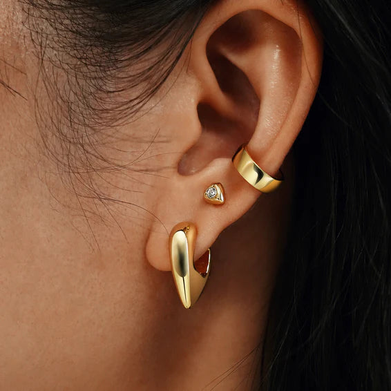 Close-up of an ear wearing gold earrings with a dark background