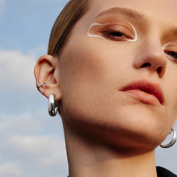 Close-up of a person wearing silver hoop earrings with a blurred sky background