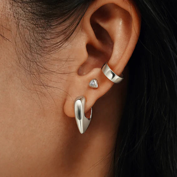 Close-up of an ear wearing silver hoop earrings with a dark background