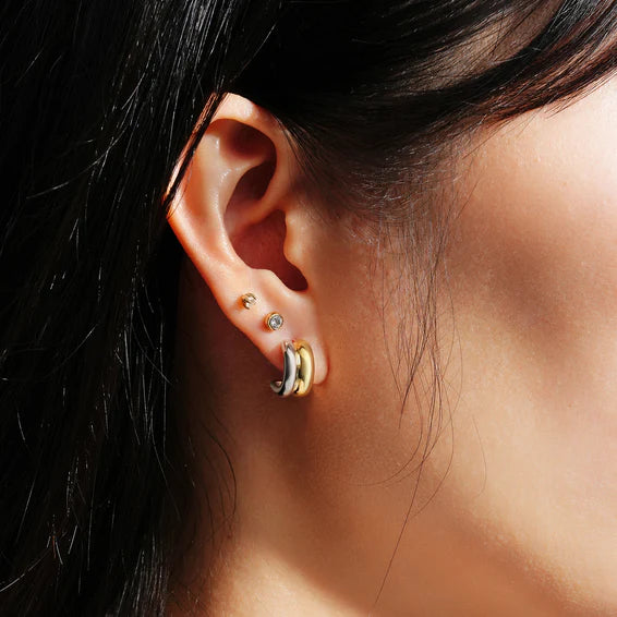 Close-up of an ear with gold hoop earrings and a small stud.