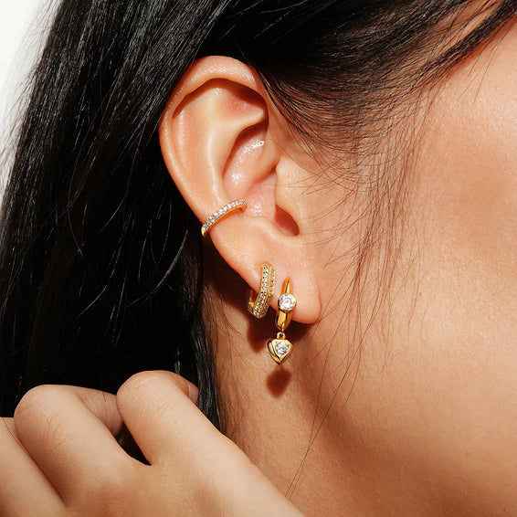 Close-up of an ear wearing gold hoop earrings with clear gemstones.