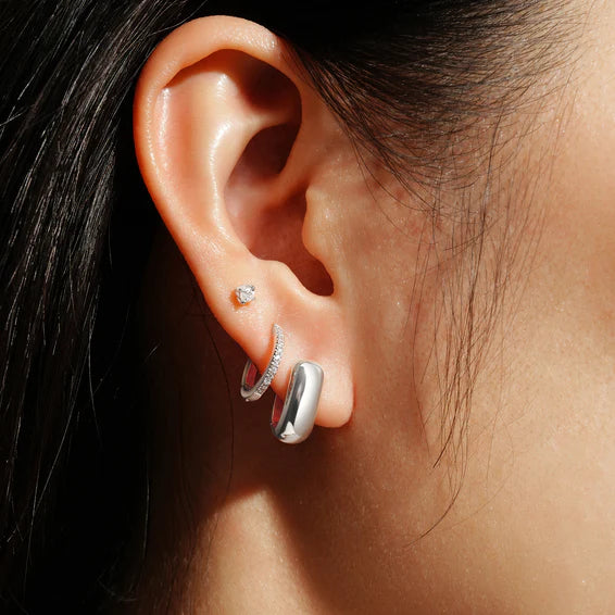 Close-up of an ear wearing silver hoop earrings with a blurred background