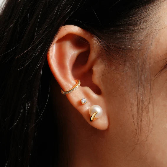 Close-up of an ear wearing gold and pearl earrings with a dark background
