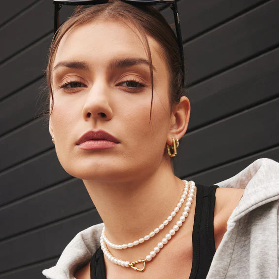 Woman wearing pearl necklaces and gold earrings against a black background