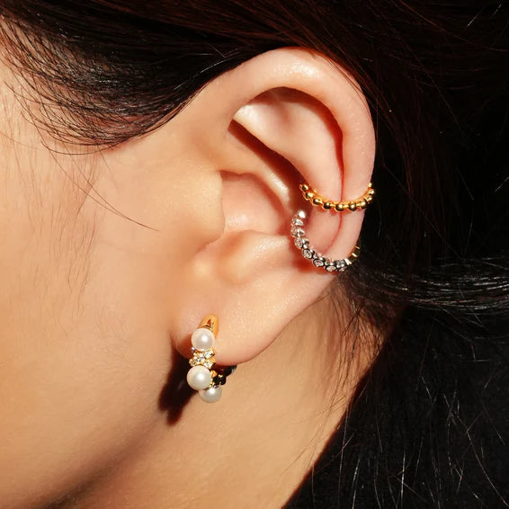 Close-up of an ear wearing gold hoop earrings with pearls.