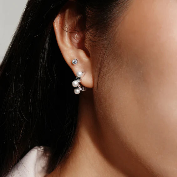 Close-up of an ear wearing pearl stud earrings with a neutral background