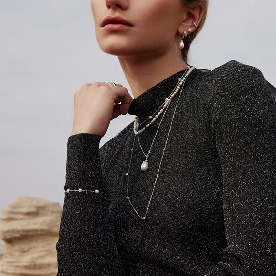 Woman wearing a black textured sweater with layered pearl necklaces against a neutral background