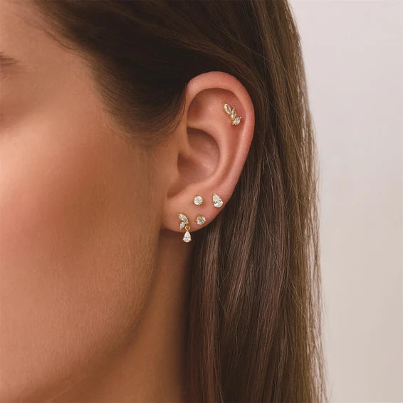 Close-up of an ear wearing multiple diamond earrings on a neutral background