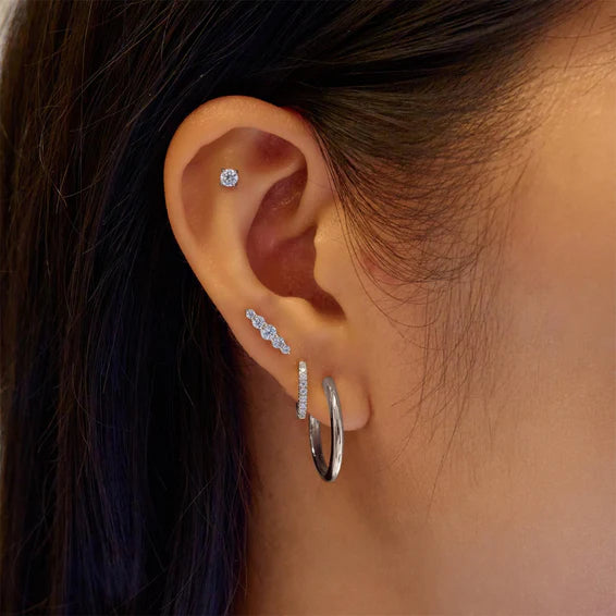 Close-up of an ear wearing multiple silver earrings with a blurred background