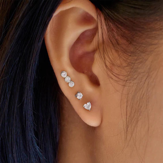 Close-up of an ear wearing multiple diamond earrings with dark hair in the background