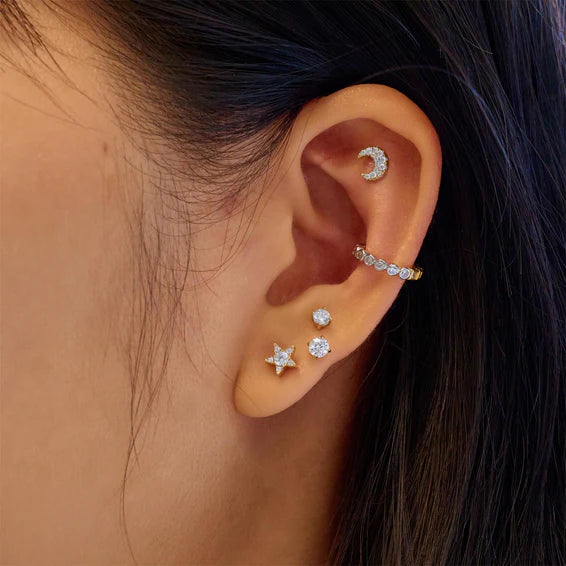 Close-up of an ear wearing multiple diamond earrings with a dark background