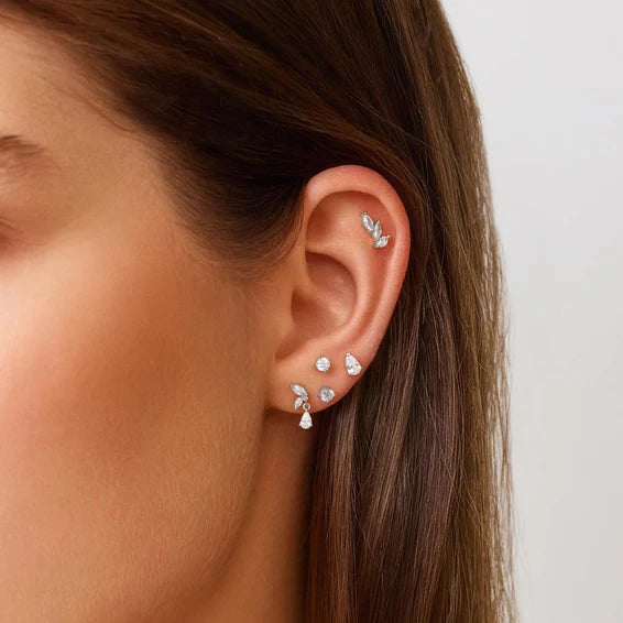 Close-up of an ear wearing multiple diamond earrings on a neutral background