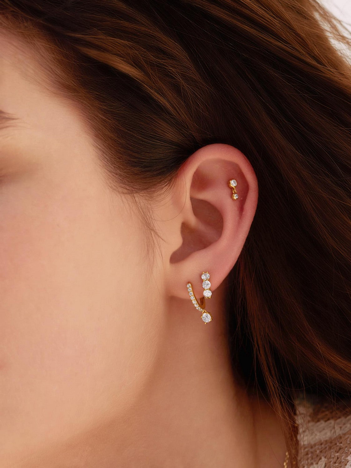 Close-up of a person wearing gold hoop earrings with small diamonds.
