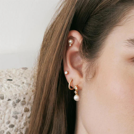 Close-up of a person wearing pearl earrings with a neutral background