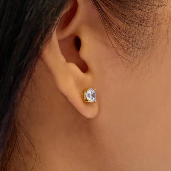 Gold earring with a clear gemstone worn by a person