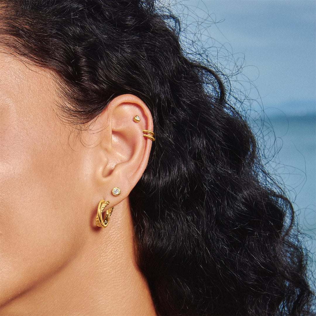 Close-up of a person wearing gold earrings with a blurred natural background
