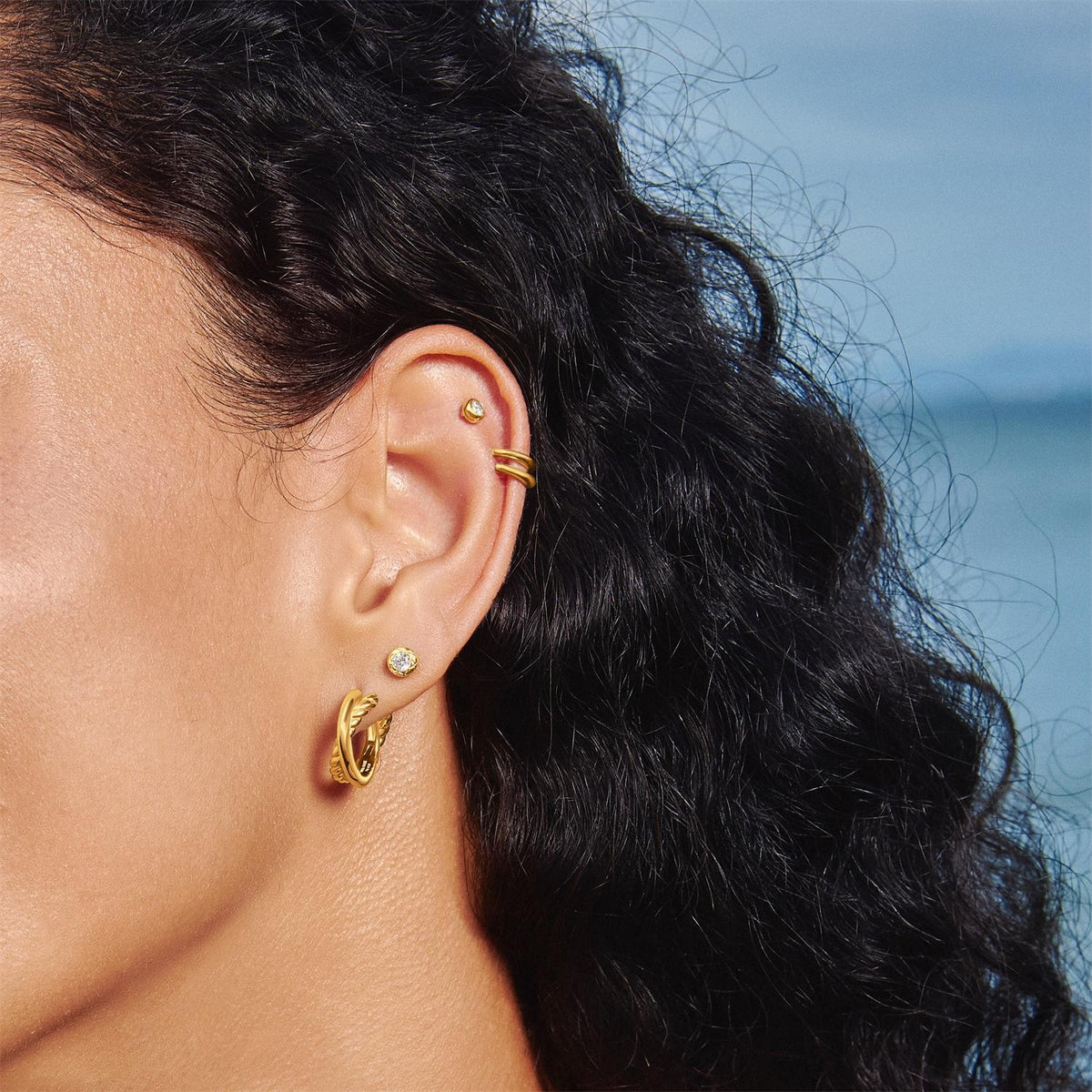 Close-up of a person wearing gold earrings with a blurred natural background