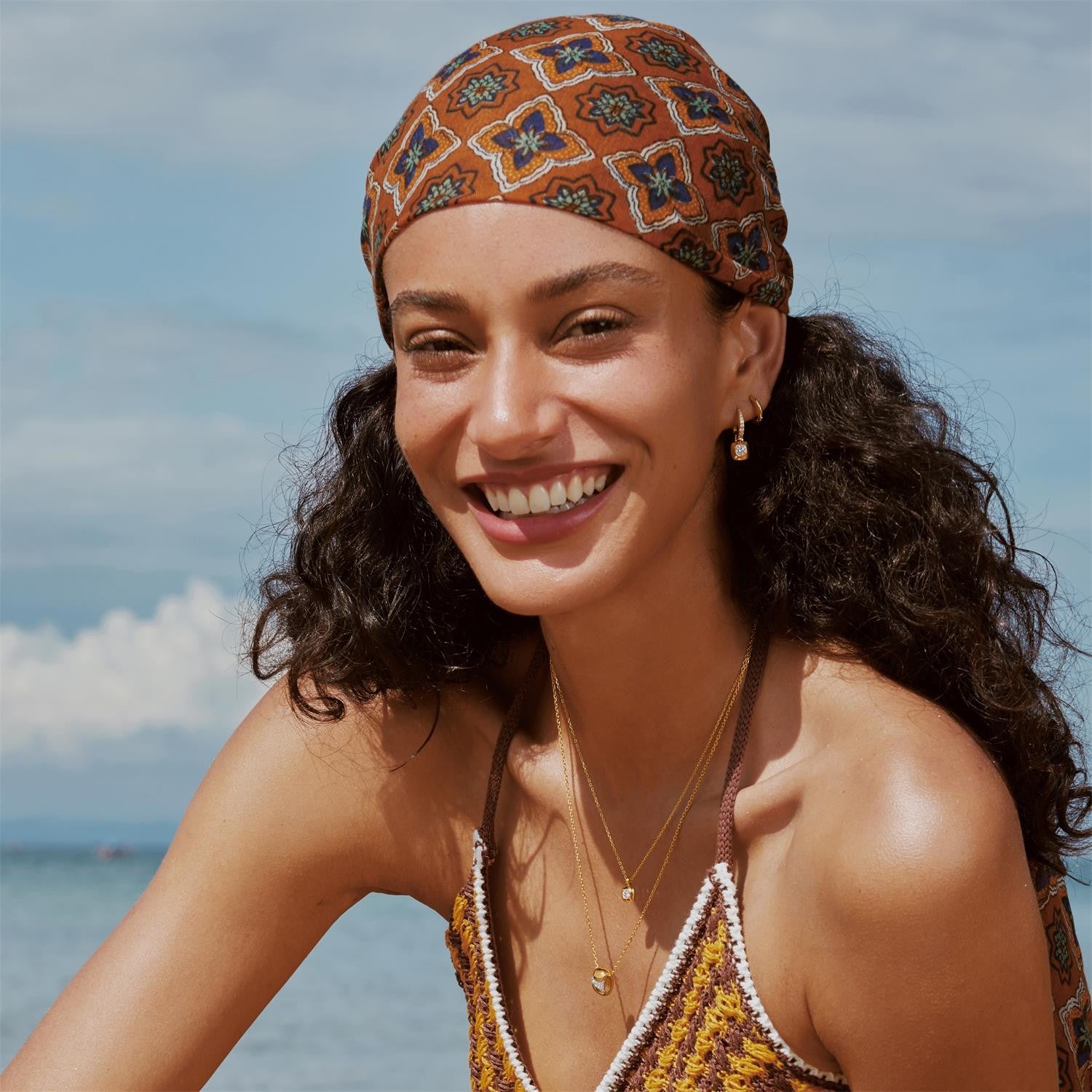 Woman wearing a patterned headscarf and smiling on a beach