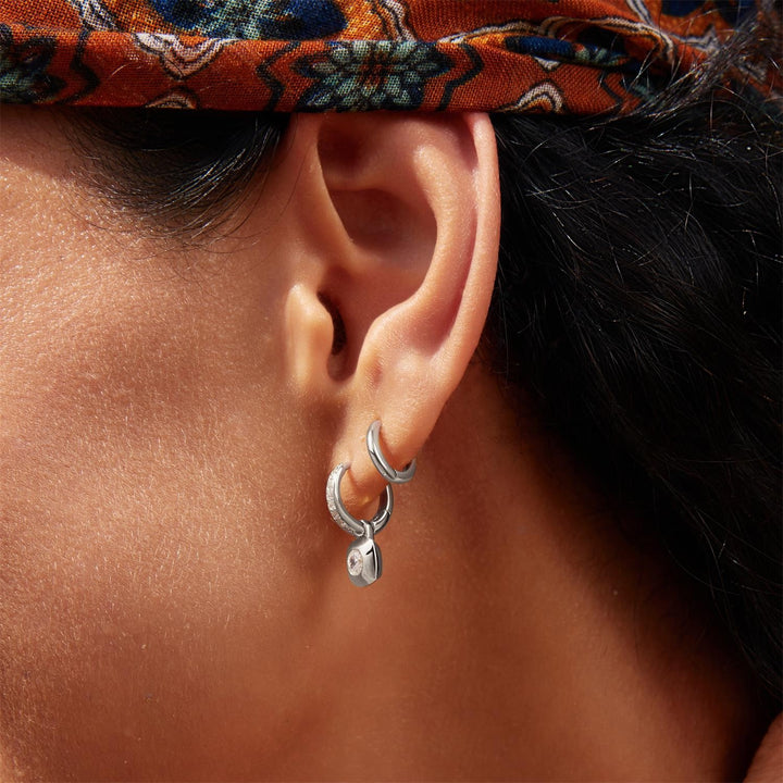 Close-up of an ear wearing silver hoop earrings with a patterned headband.
