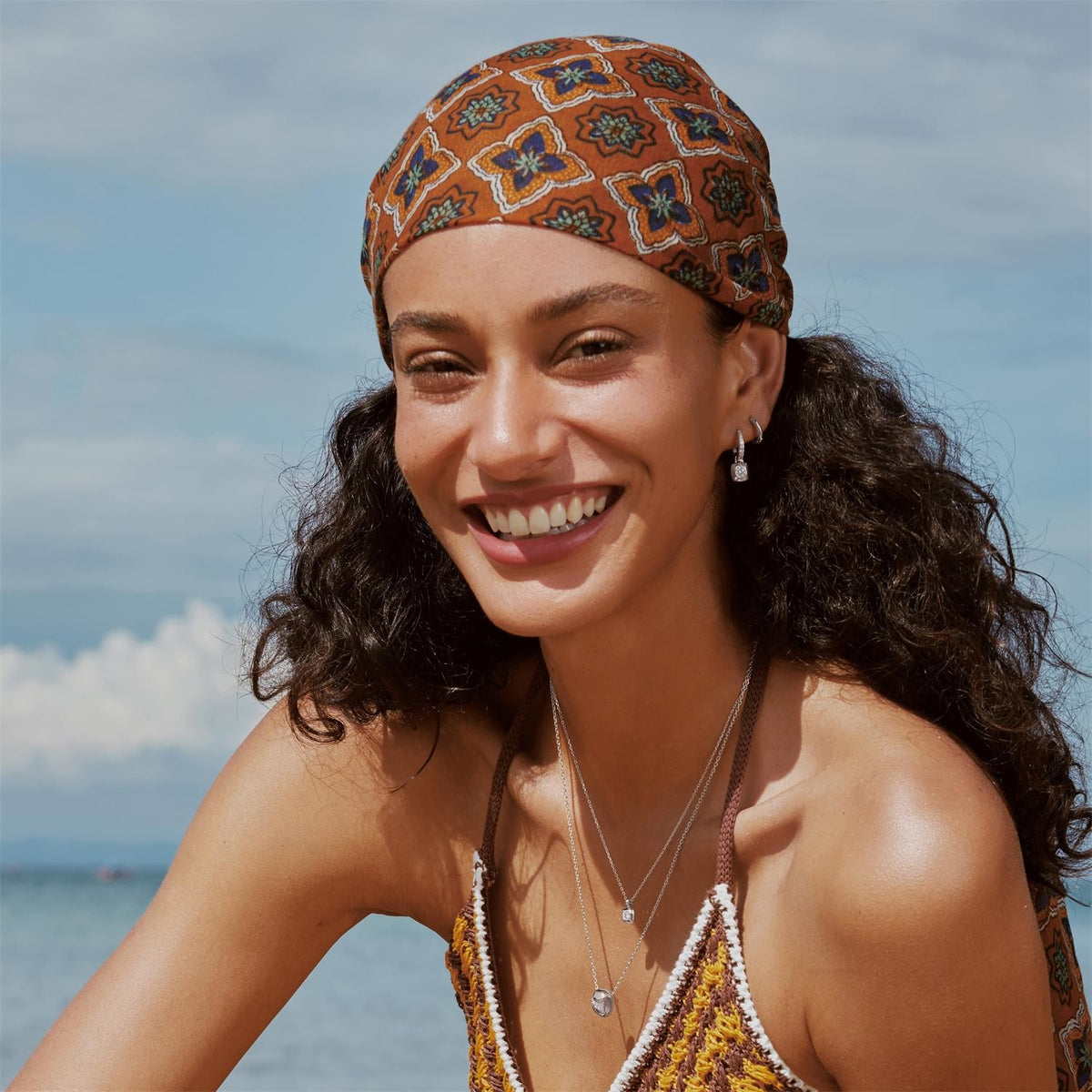 Woman wearing a patterned headscarf and smiling with a beach in the background