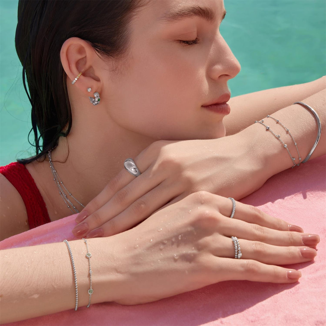 Woman with silver jewelry including rings and bracelets by a pool.