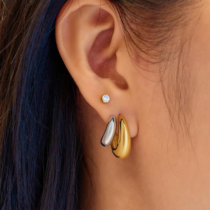 Close-up of an ear wearing a gold and silver earring with a blue gemstone.