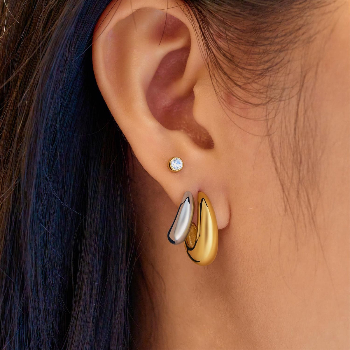 Close-up of an ear wearing a gold and silver earring with a blue gemstone.