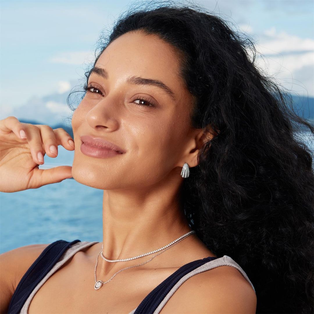Woman with long dark hair and earrings against a blue sky background