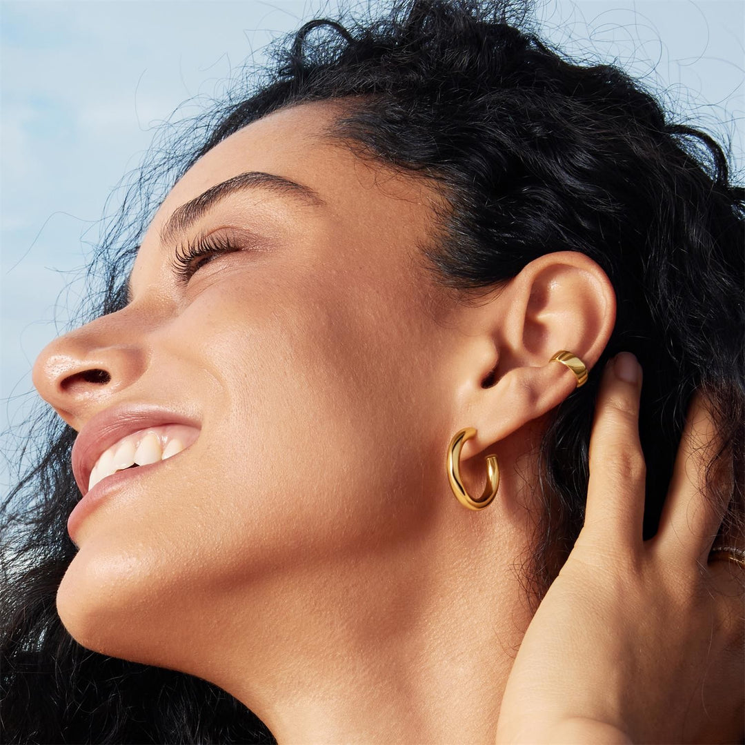 Close-up of a woman wearing gold hoop earrings with a blurred background