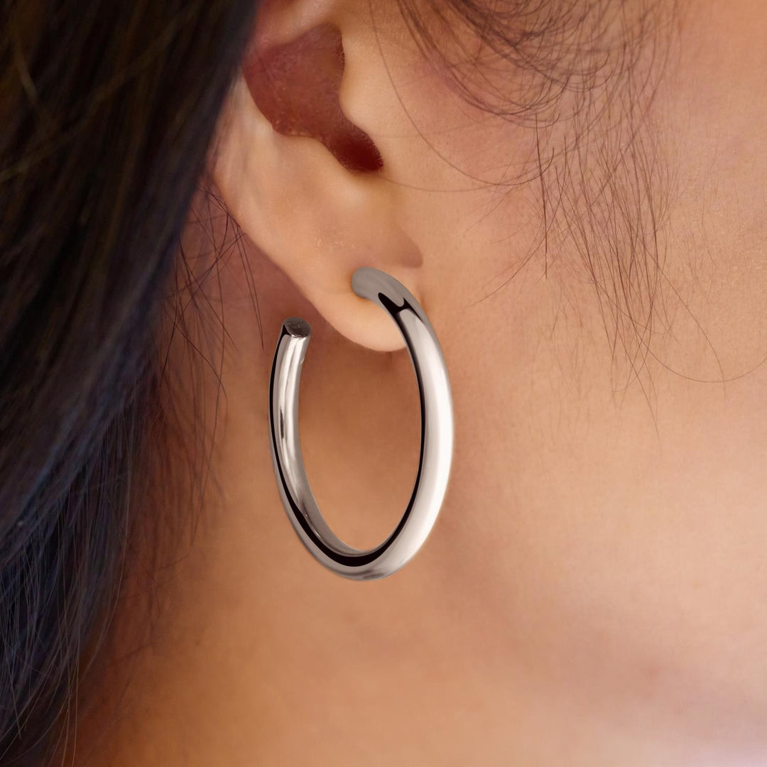 Silver hoop earring worn on an ear with a neutral background