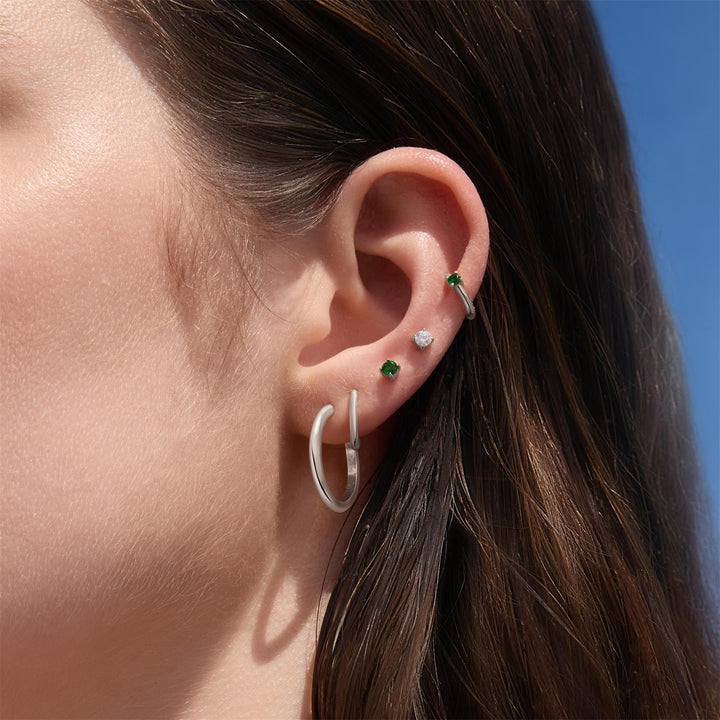 Close-up of an ear wearing multiple earrings with a clear blue sky background