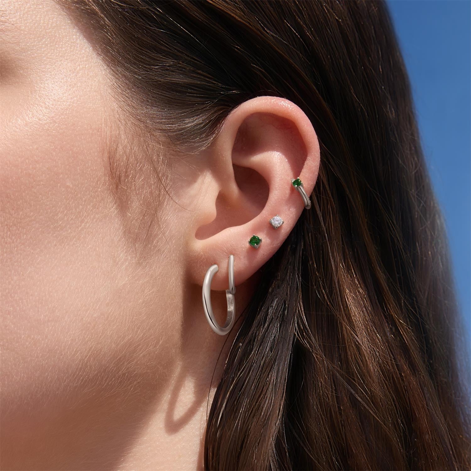 Close-up of an ear wearing multiple earrings with a clear blue sky background
