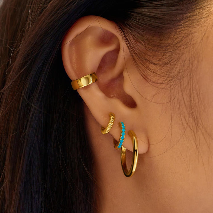 Close-up of an ear with gold hoop earrings and a turquoise stone.
