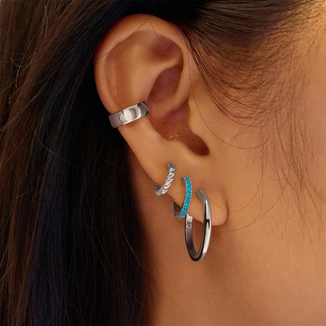 Close-up of an ear wearing multiple silver hoop earrings with a turquoise stone.