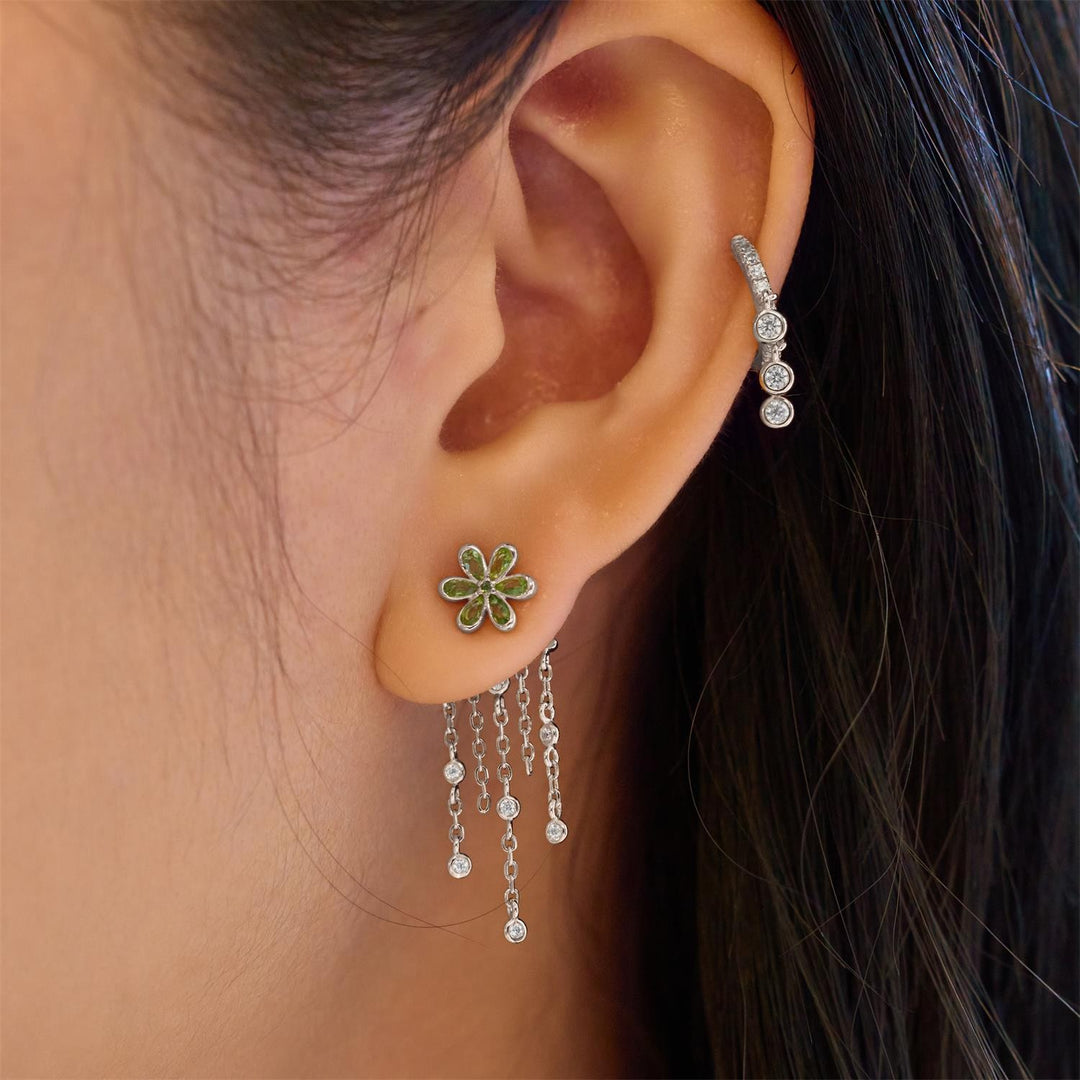 Close-up of an ear wearing a floral earring with dangling charms.