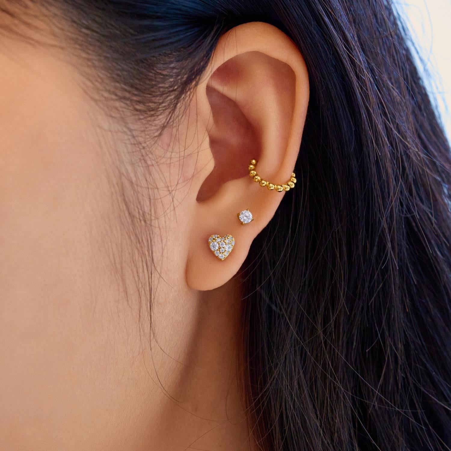 Close-up of an ear wearing gold and diamond earrings with dark hair.