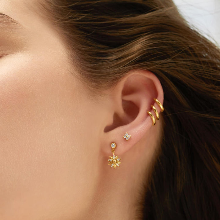 Close-up of a person's ear wearing gold earrings with a neutral background